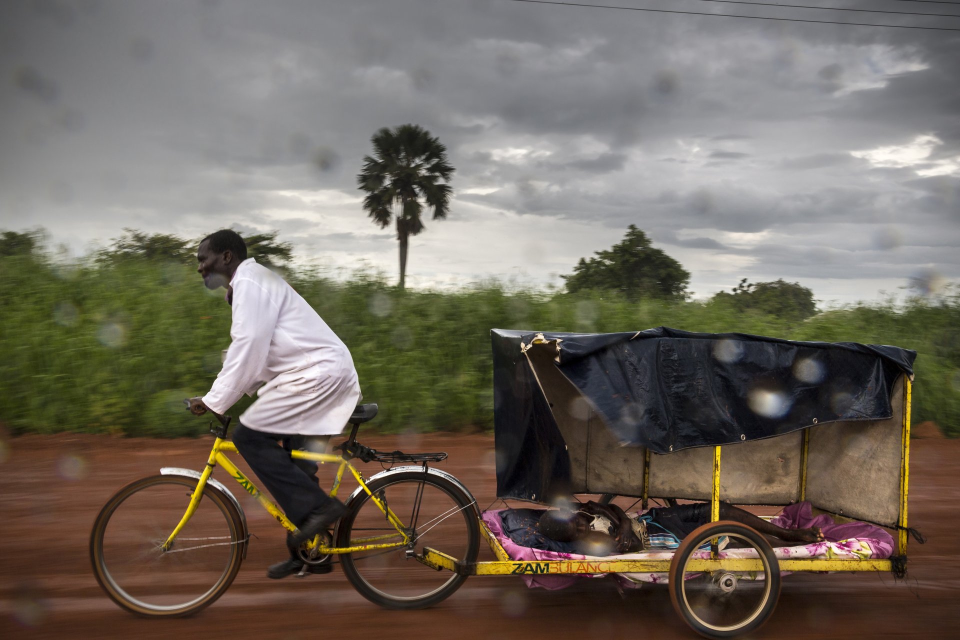 A volunteer community health worker uses his bicycle ambulance to transport a young boy with malaria to the nearest clinic