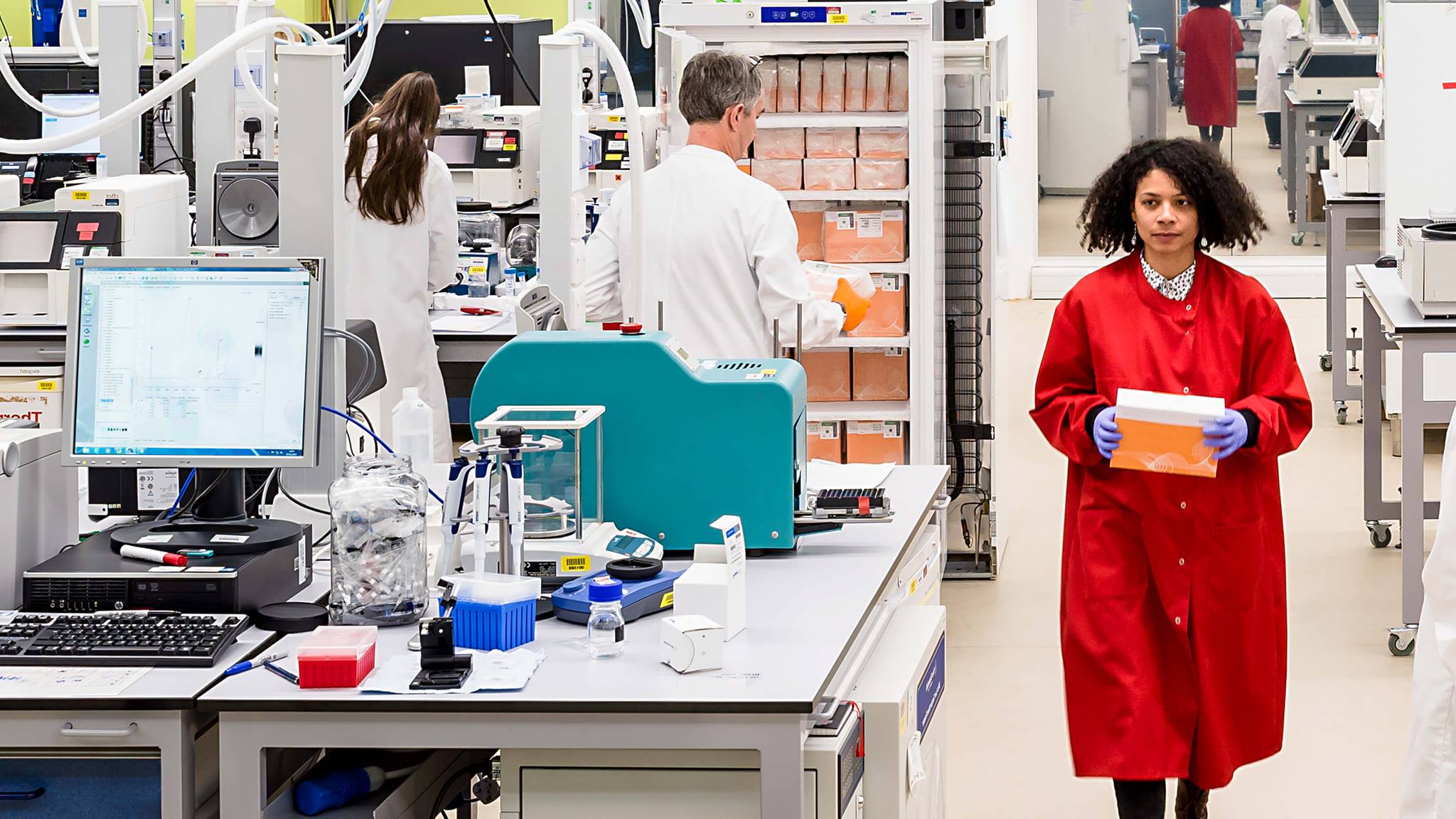 A researcher wearing a red lab coat in the Sequencing Centre at the Wellcome Sanger Institute