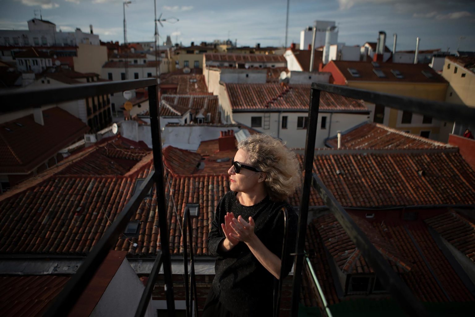 A woman stands atop the roof of her house.