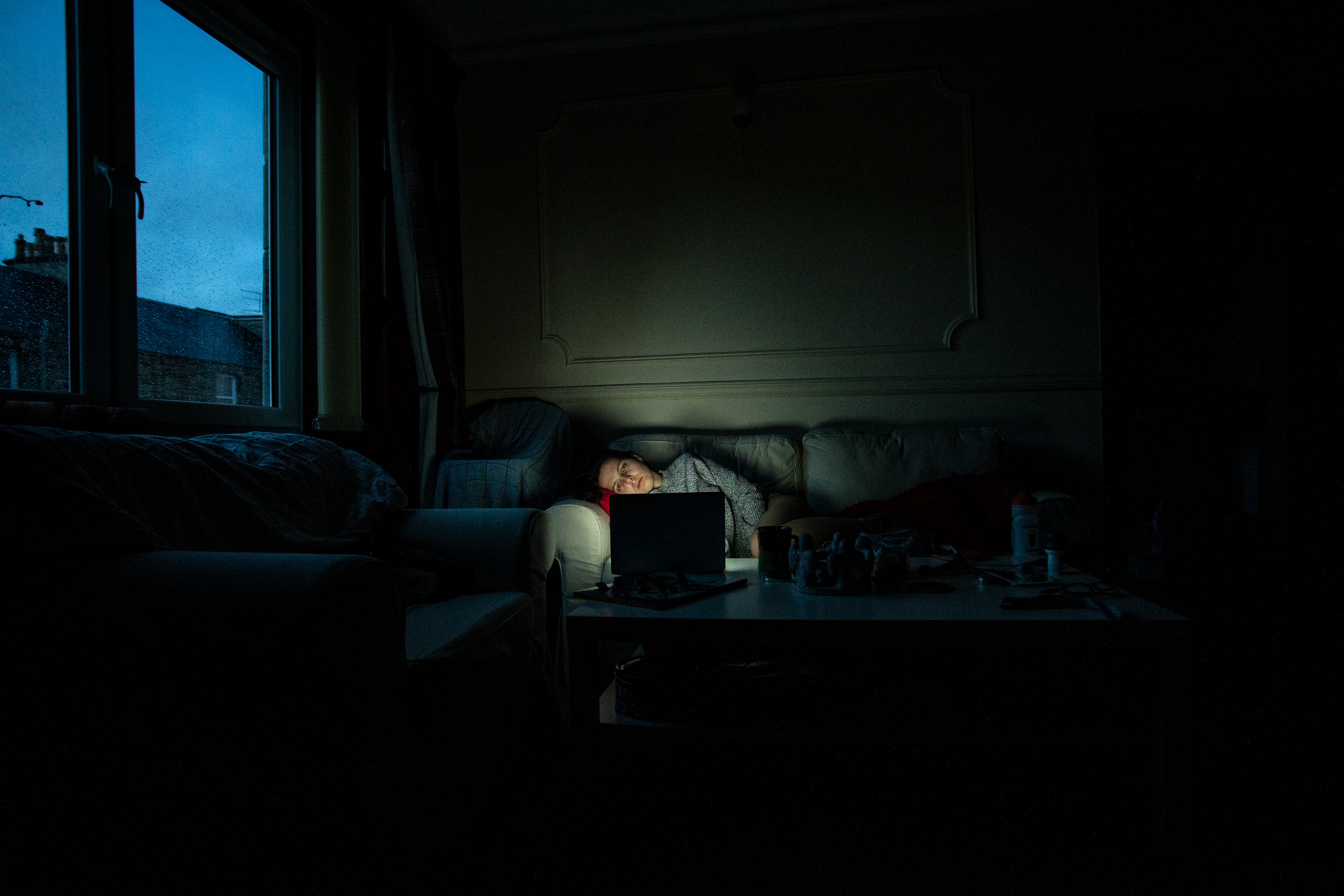 A self-portrait of the photographer laying on a sofa in a dark room watching a laptop.