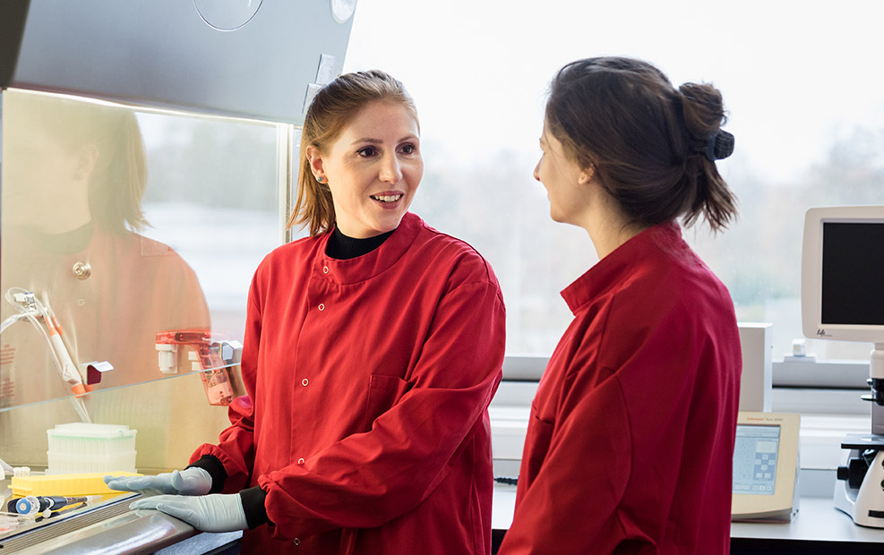 Two female researchers in red lab coats talking