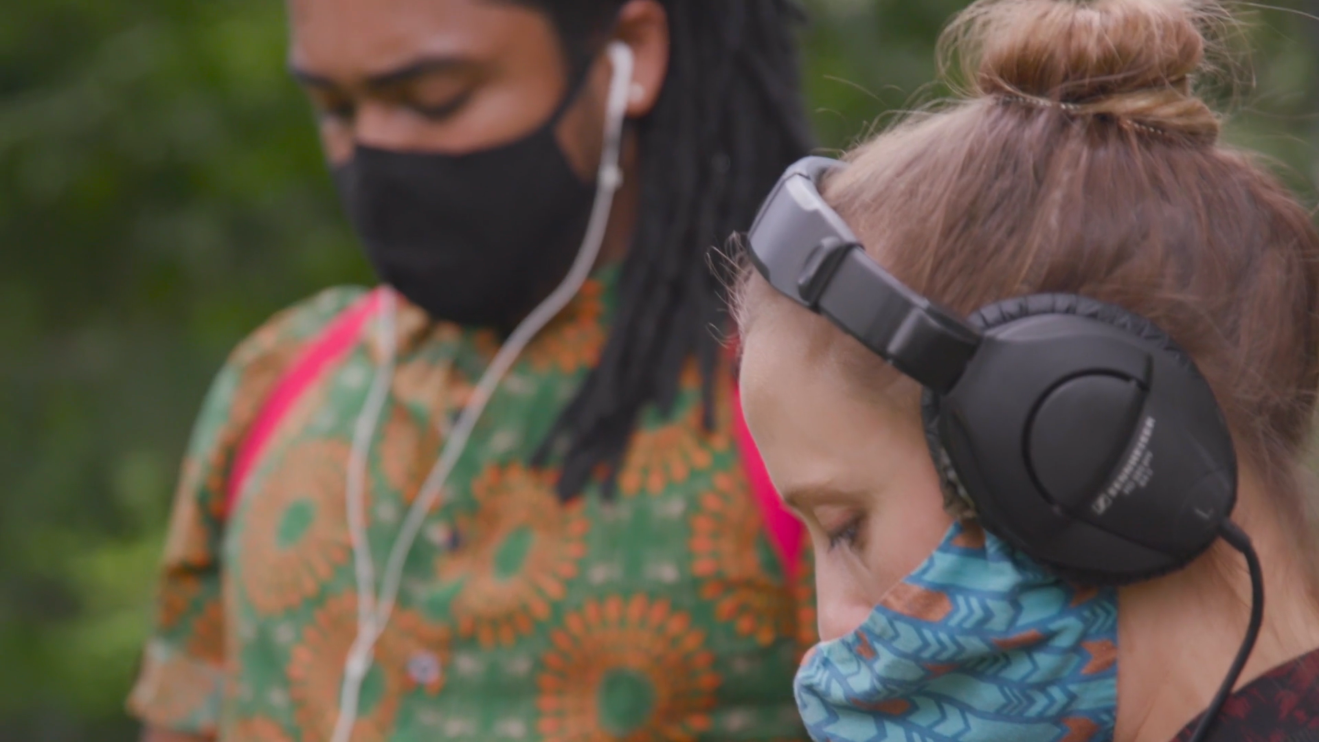 A man and a woman wearing headphones and face masks, listening to audio