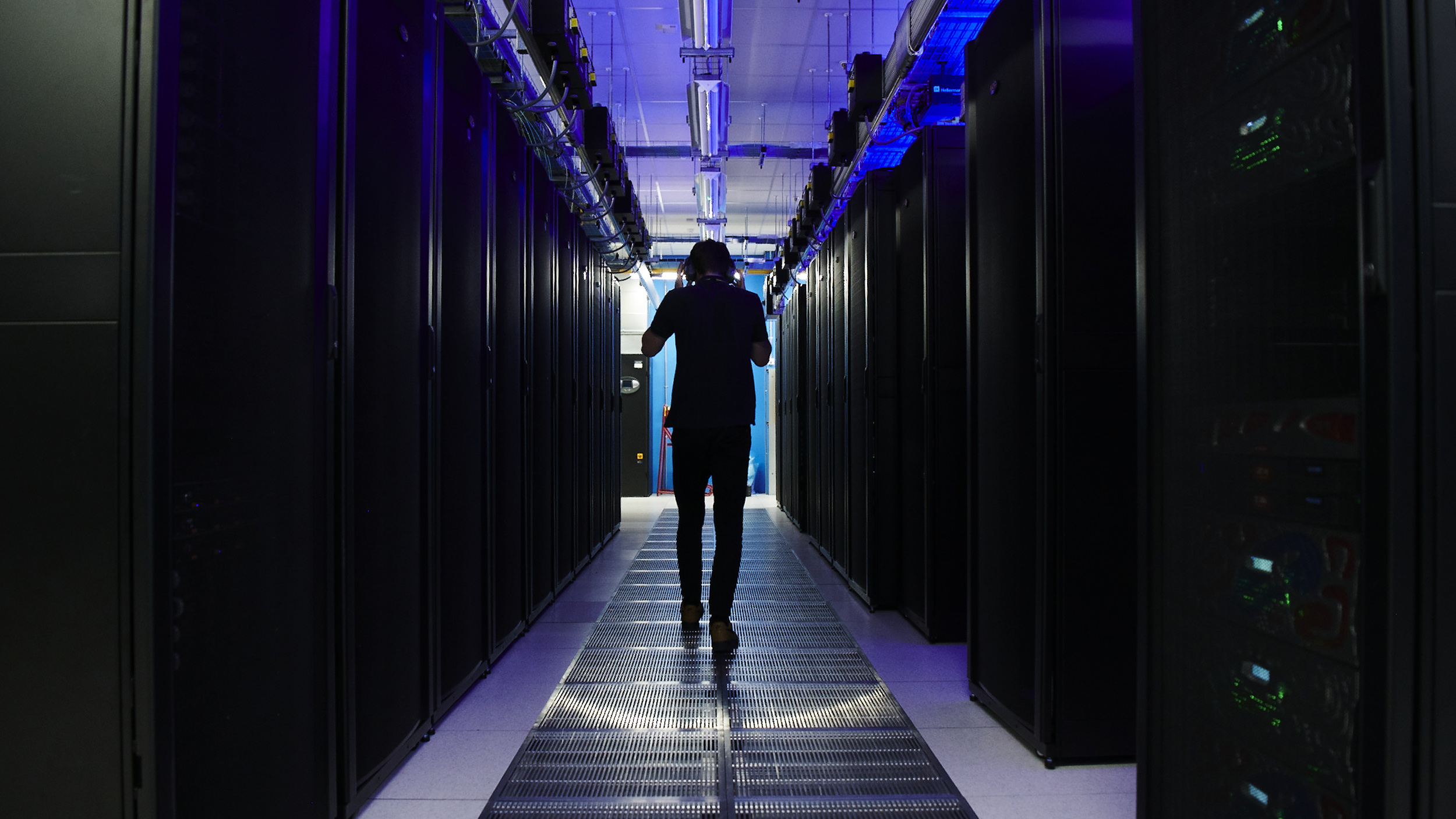 A man walks in a room full of data servers.