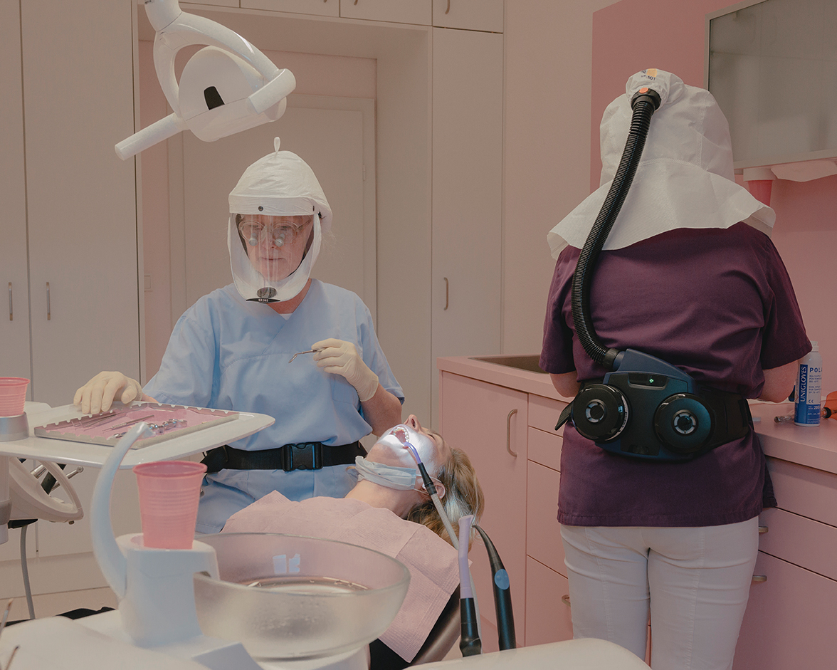 A dentist and patient both wear extensive PPE during a dental appointment.