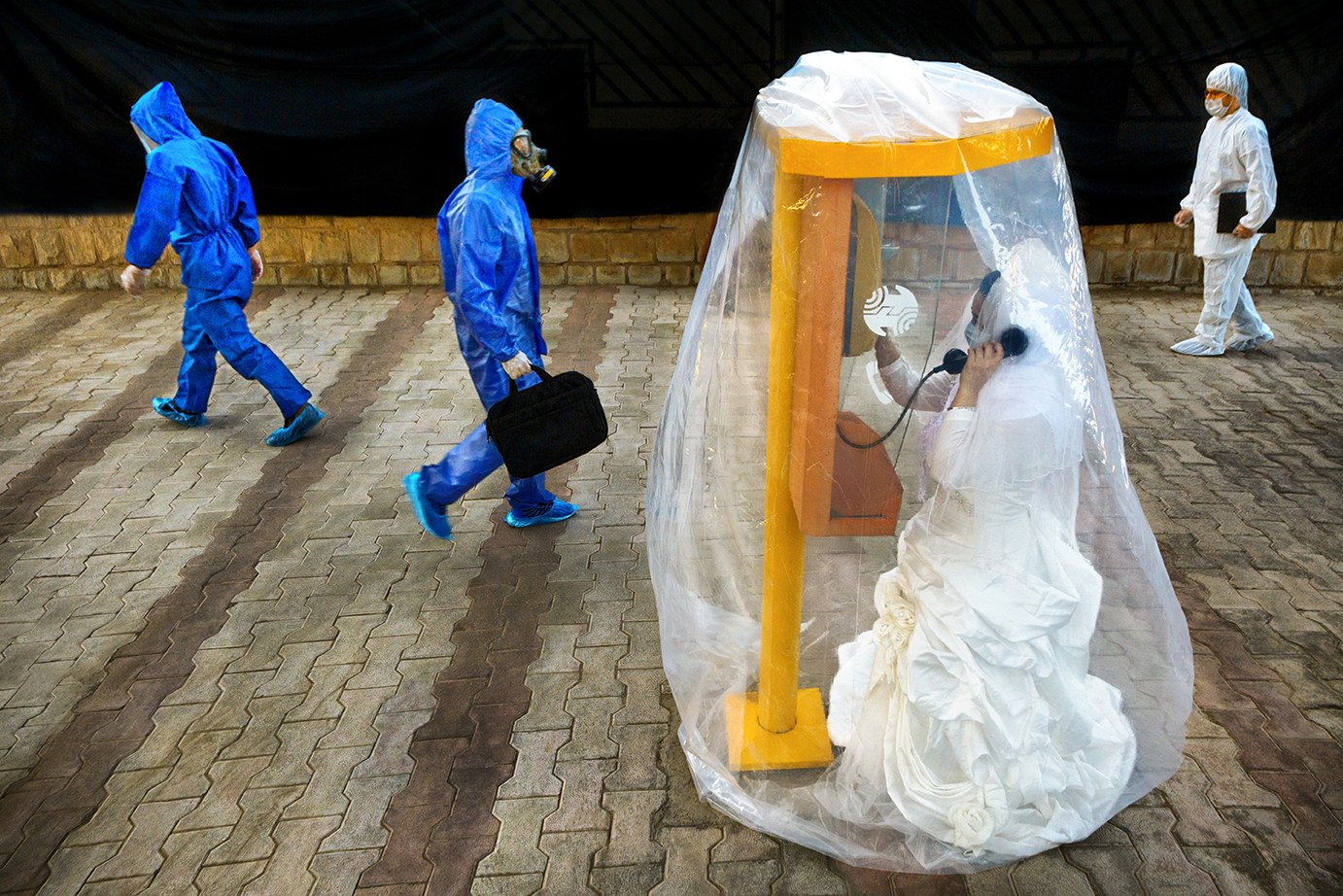 A staged image depicting a woman in a wedding dress, calling her groom from inside a protective bubble. 