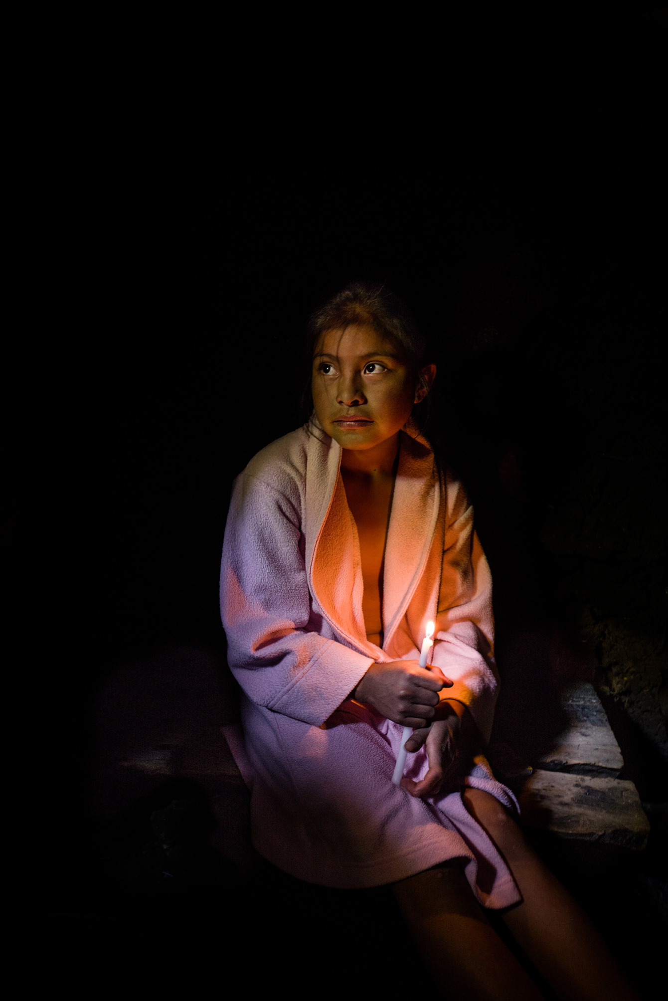 Petrona, age ten, sits on a wooden bench inside a chuj, a Mayan steam bath.