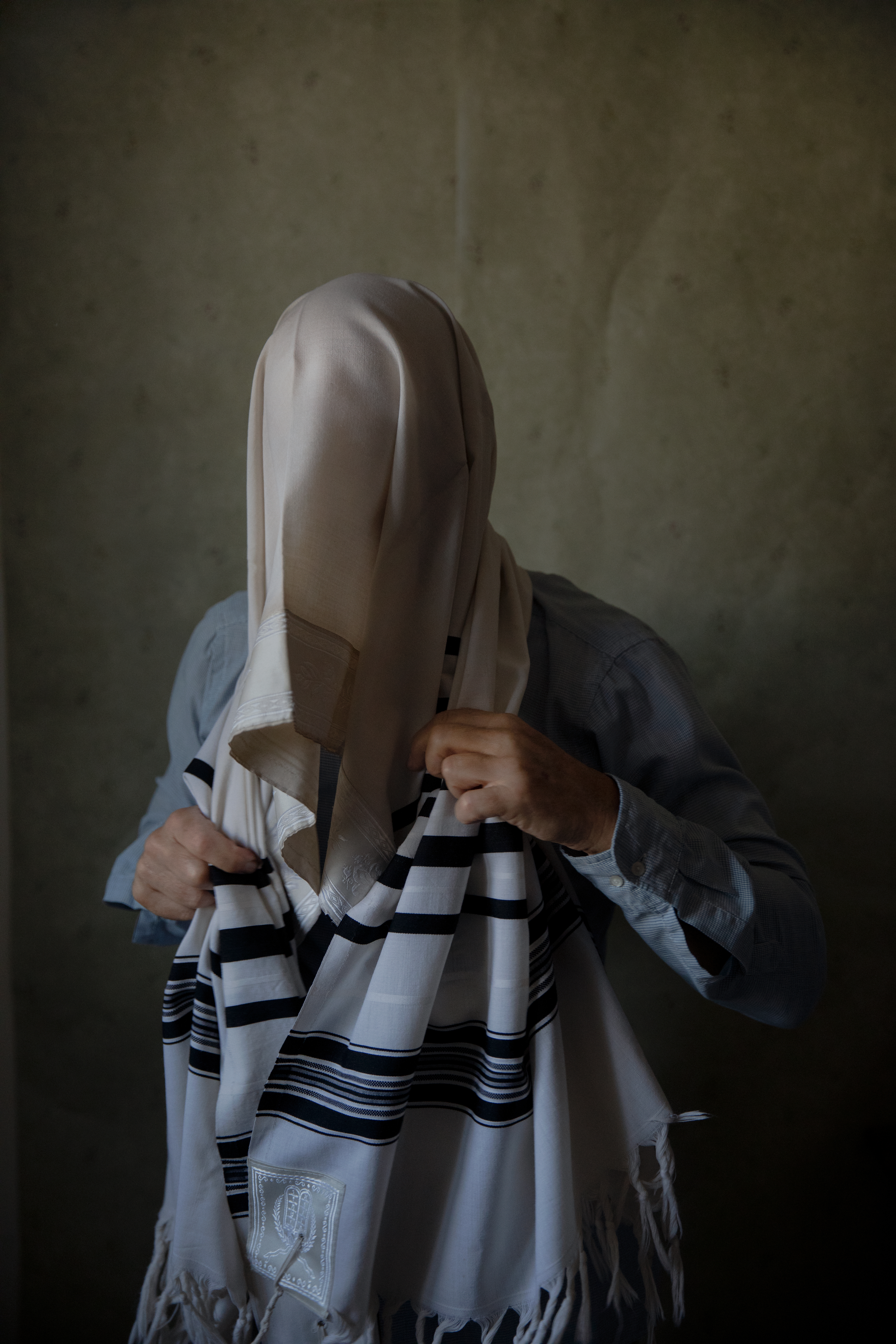 A man poses wrapped in his tallit prayer shawl to symbolise the way he conceals his identity from his religious community in Israel.