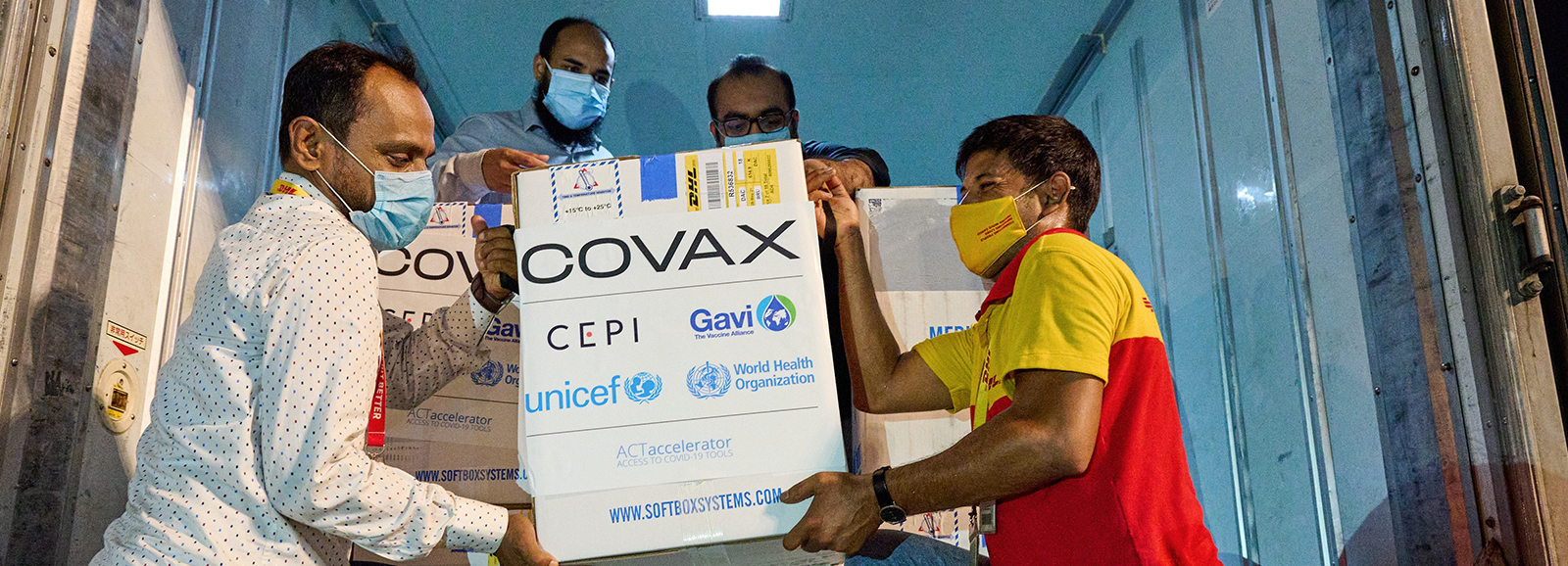 A group of men unload a box that says 'COVAX' from a truck.