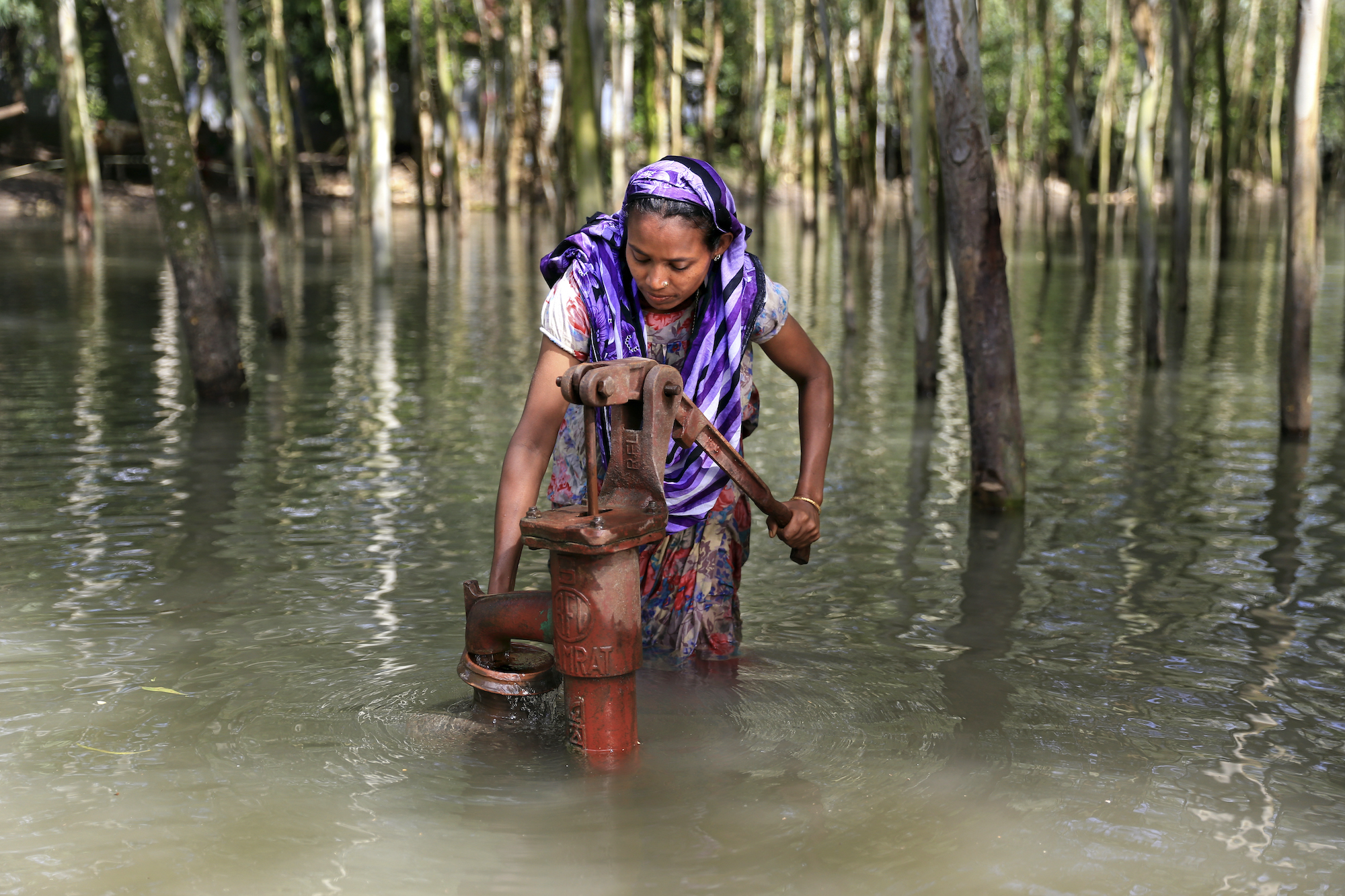 A woman stands knee-deep in flood water collecting safe drinking water from a hand pump. Waterborne diseases are caused by drinking or coming into contact with contaminated water.