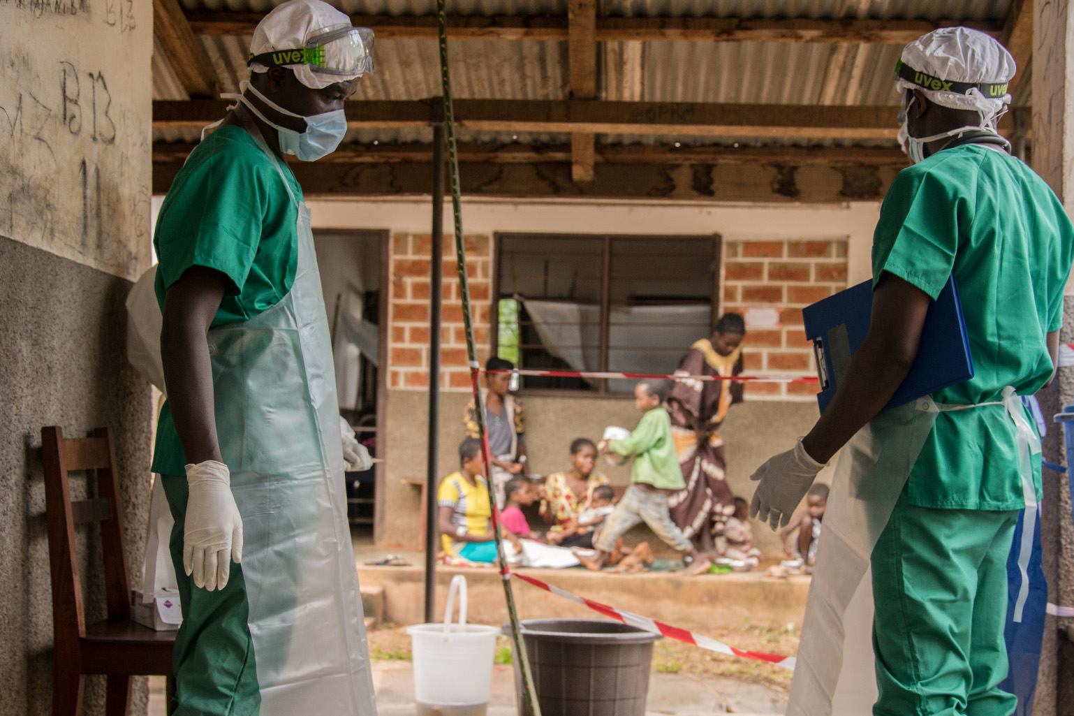 Two medical staff outside of a mpox quarantine area in the Central African Republic with children visible in the background