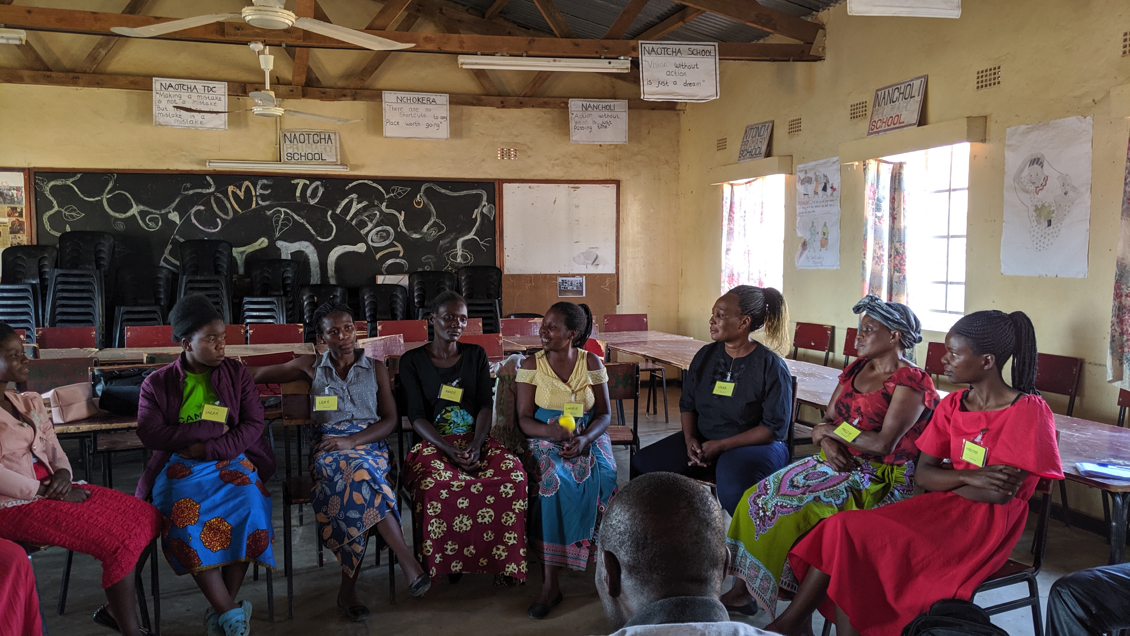 A group of women sit together inside a classroom discussing.