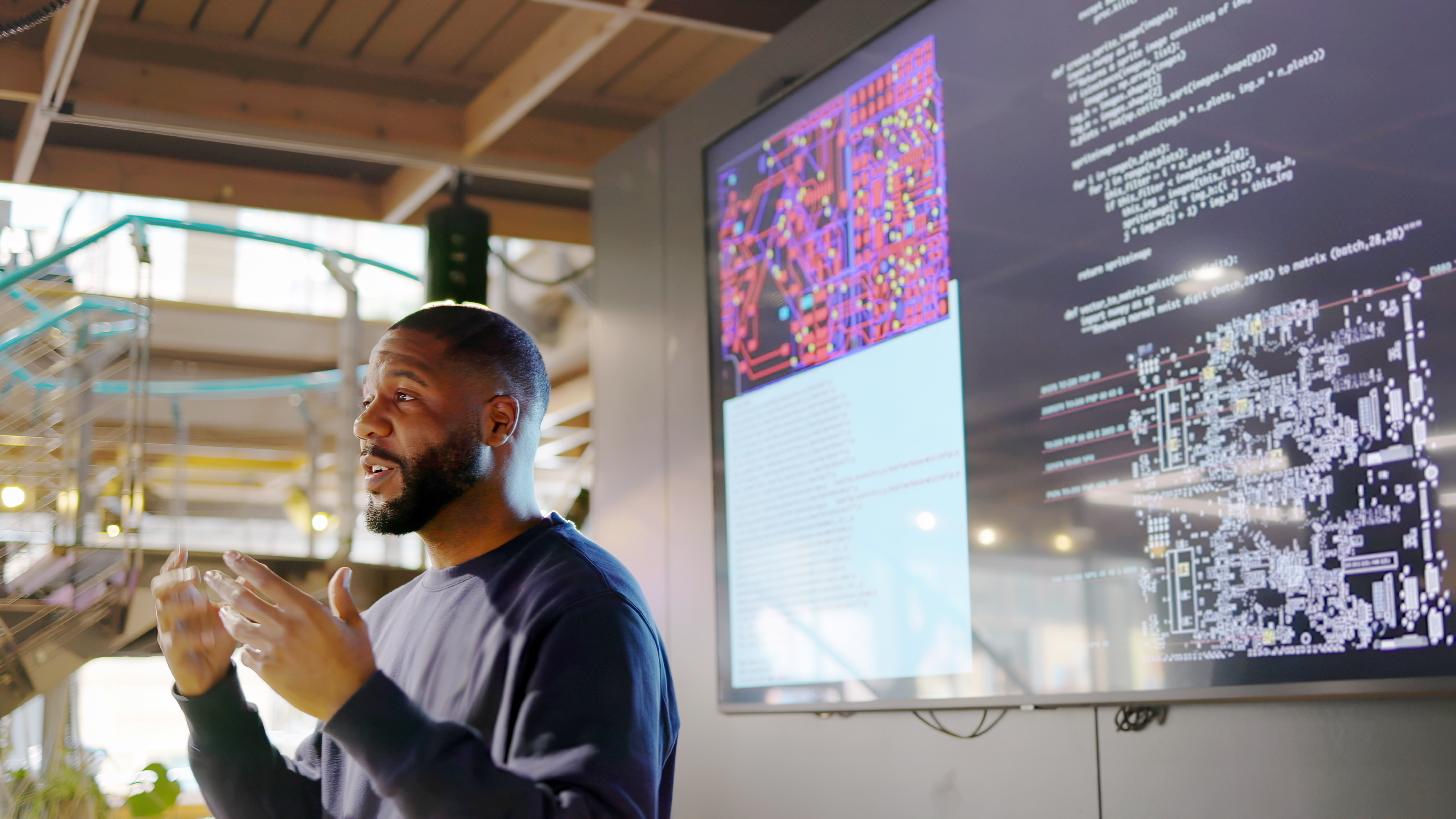 A man is presenting in front of a large screen that shows some data and colourful imagery.