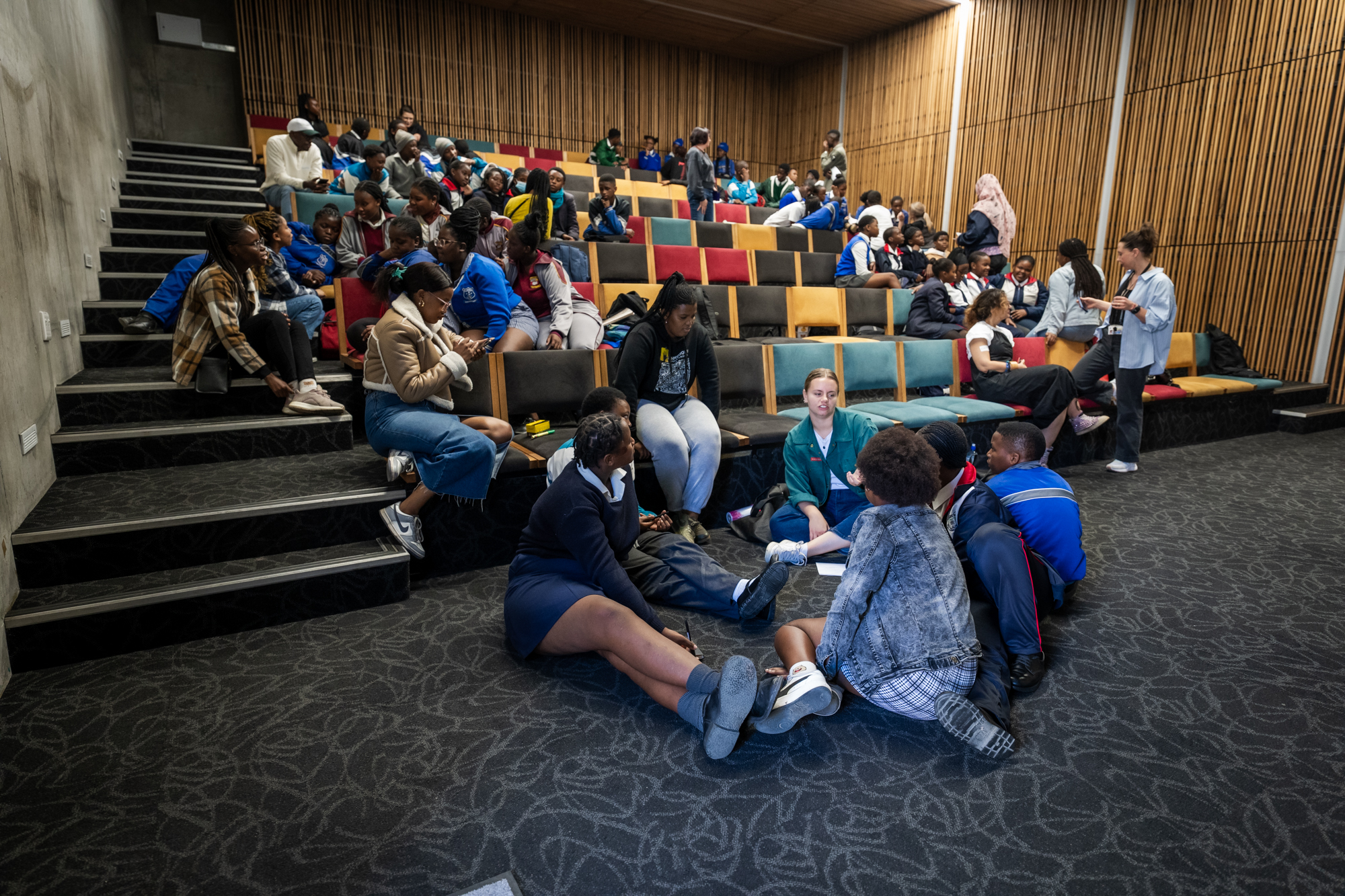 Wide shot of young learners talking to one another inside a theatre-like conference room during an AMR workshop in Khayelitsha, South Africa.