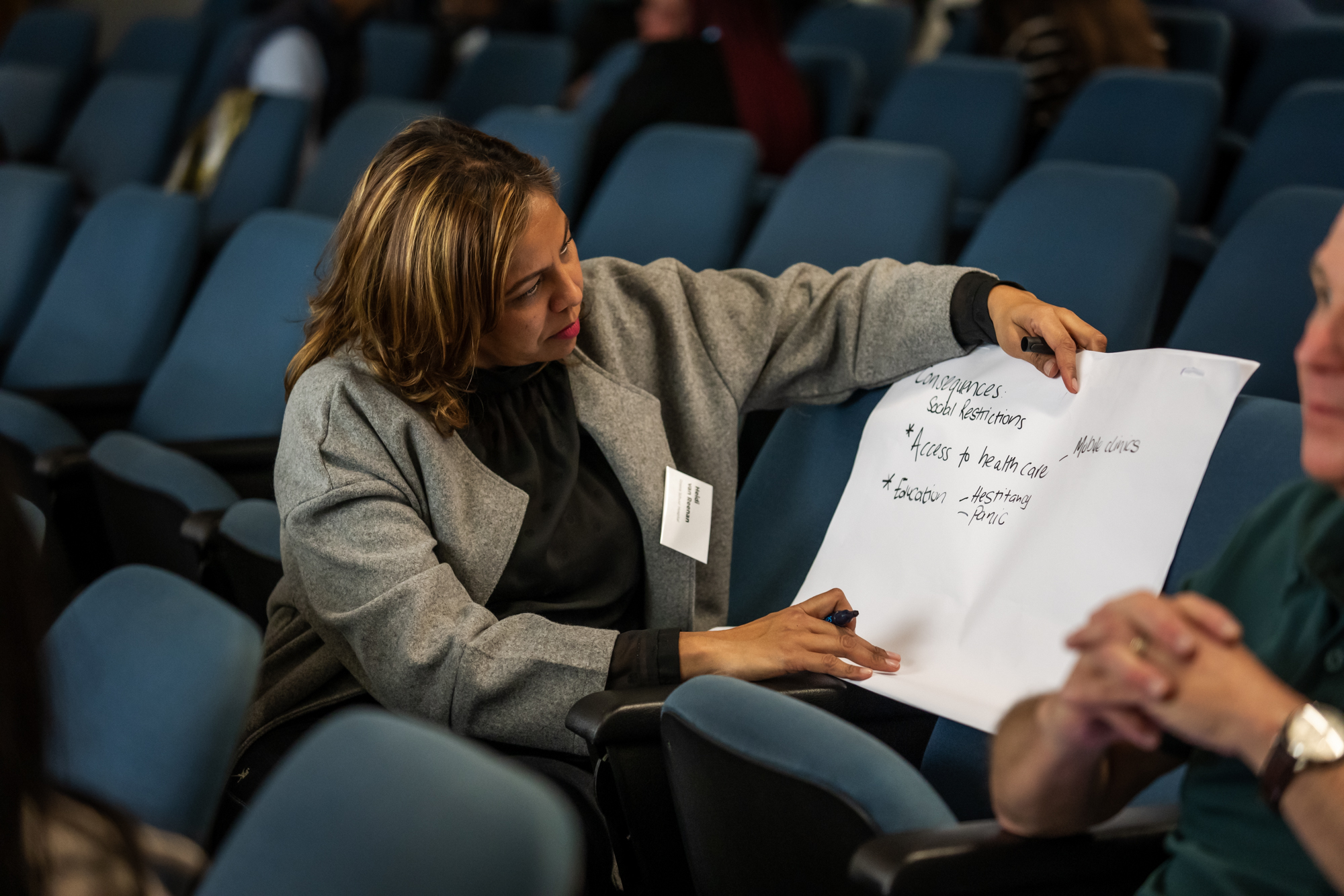 A woman, sitting down in theatre-like conference room, writes on a piece of paper during an AMR workshop.