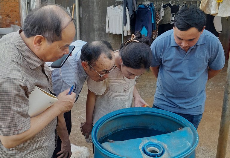 People are seen inspecting a barrel of water used for informal storage.