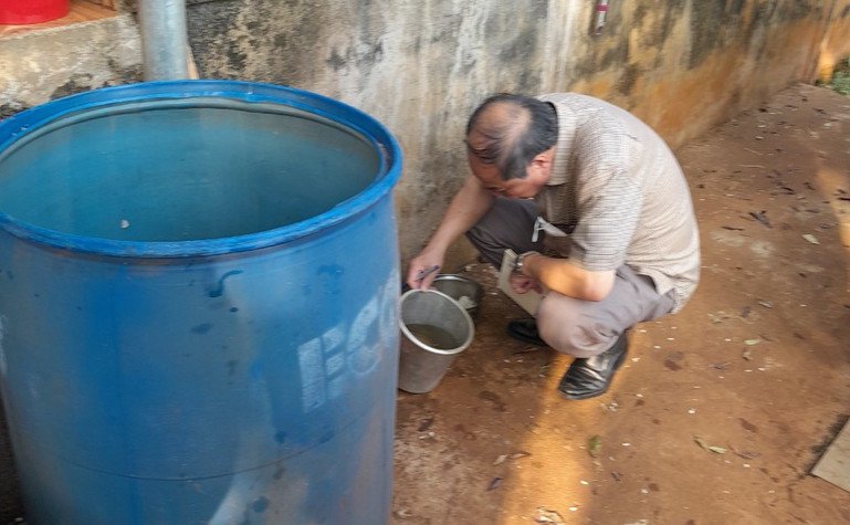 A man squats on the ground and tilts a small container with water.