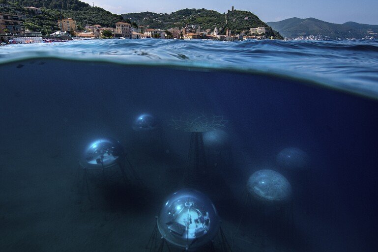 The depth of the biospheres, between six and twelve metres beneath the sea’s surface, allows the plants the sunlight they need. The town of Noli in Liguria, Italy is visible on the mainland.