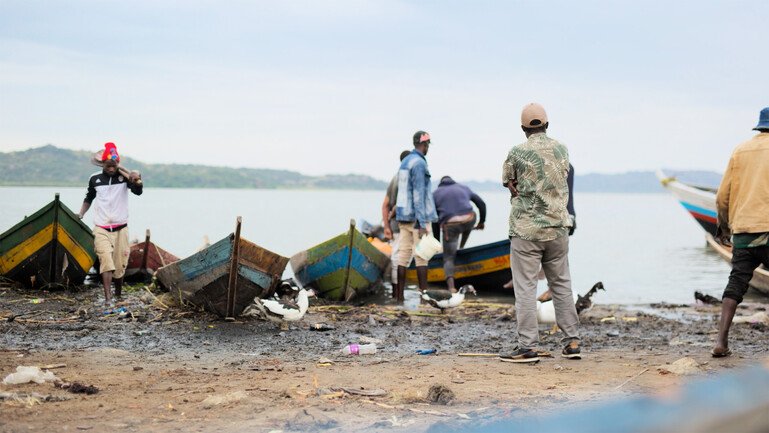 People stand among wooden fishing boats on the shore of Lake Victoria.