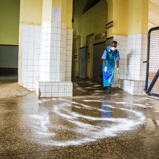 Cleaner using chlorine powder to disinfect emergency entrance to Connaught Hospital, Sierra Leone