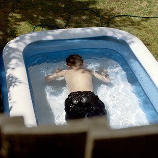 A boy holds his breath underwater in a paddling pool