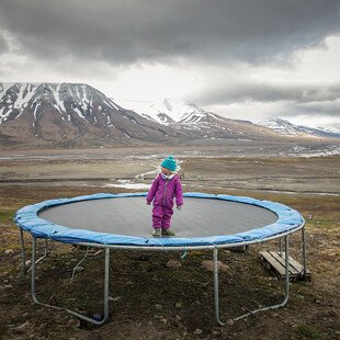 A girl stands on a trampoline in the middle of a mountainous landscape.