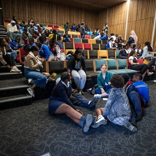 Wide shot of young learners talking to one another inside a theatre-like conference room during an AMR workshop in Khayelitsha, South Africa.