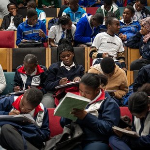 A group of young learners sitting in a theatre-like conference room. They are jotting down notes during an AMR workshop in Khayelitsha, South Africa.