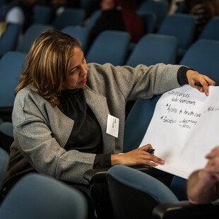 A woman, sitting down in theatre-like conference room, writes on a piece of paper during an AMR workshop.