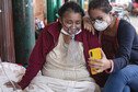 A Covid-19 patient breathing with the assistance of oxygen and her daughter sitting on a bed in a hospital talk to relatives through a mobile phone.