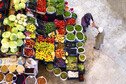 Top view of a woman and man next to colourful vegetables and fruits stands.