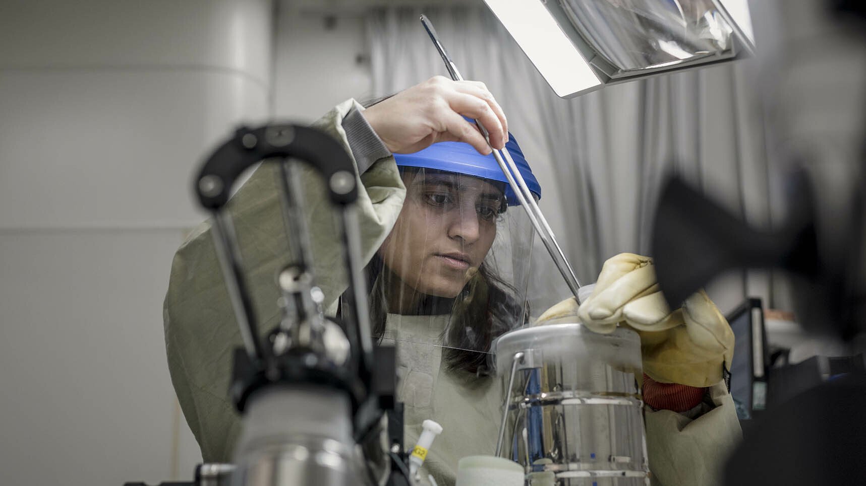 A female researcher wearing a face shield and gloves carries out research.