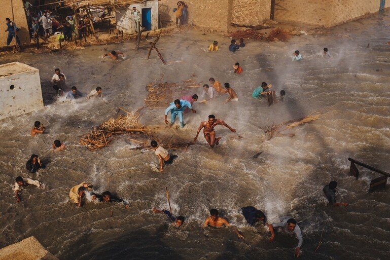 People in a flooded Pakistani village scramble for food rations as they battle the downwash from an army helicopter delivering aid