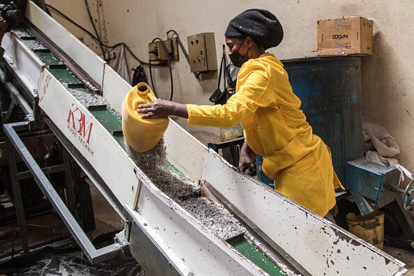 A woman in yellow protective clothing pours shredded plastics on a conveyor at a recycling plant in Nairobi, Kenya.