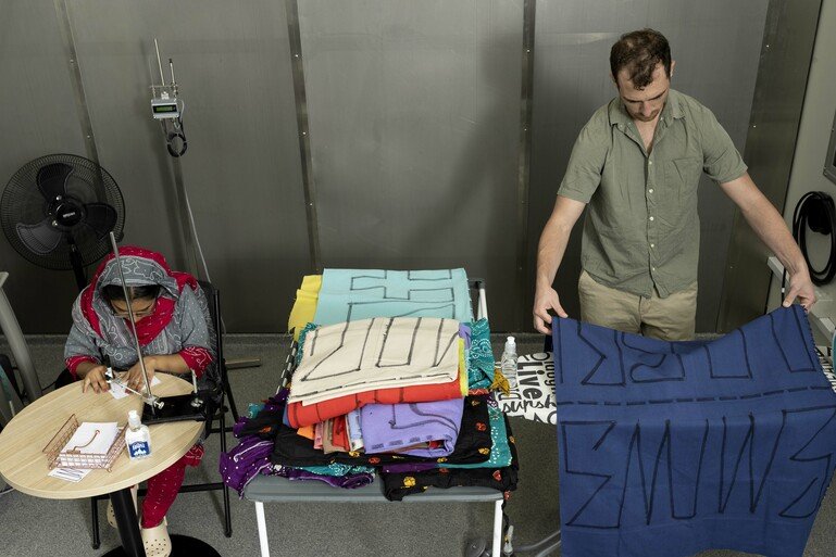 Two research volunteers in a room – one is ironing clothes and one is using a sewing machine.