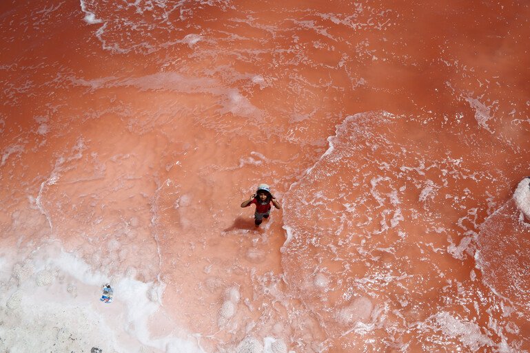 A drone photo shows a person standing in Lake Urmia. The water is a red.