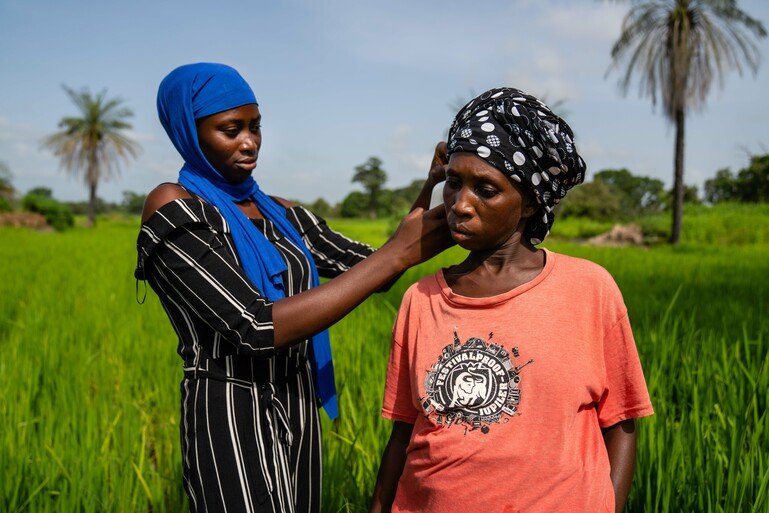 A pregnant woman farmer is looked over by another woman as they stand outside on a field.