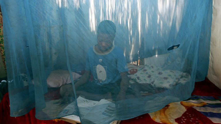 A child sits under a mosquito net in his home.