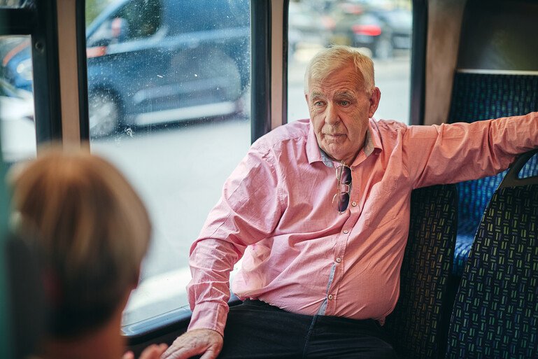 Bryan White, a participant in the RECOVERY trial, seated on public transport and speaking with another person out of focus