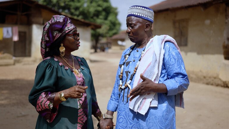 Esther Mokuwa and Chief Kallon standing together and talking on a village street in Sierra Leone.