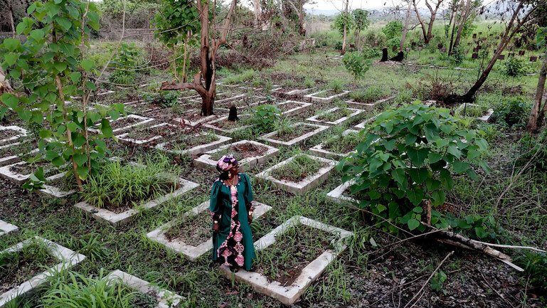 Esther Mokuwa standing among grave plots at a cemetery in Sierra Leone.