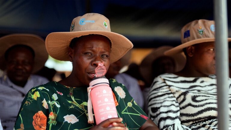 A woman wearing a sunhat drinks from a pink water bottle.