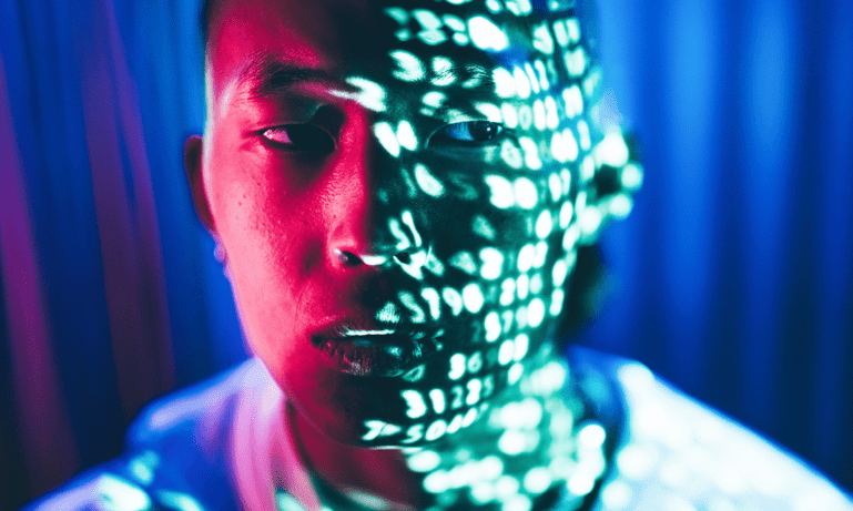 A man looks to the right, his face is illuminated by text from computer code
