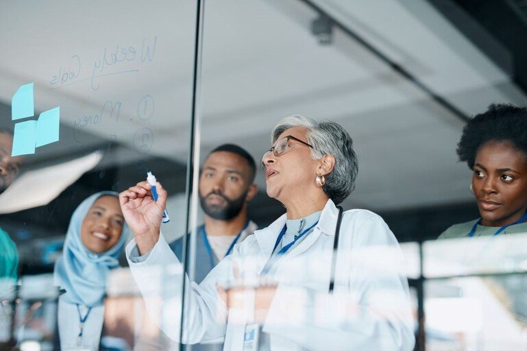 Four people in a lab looking at notes pinned to the wall