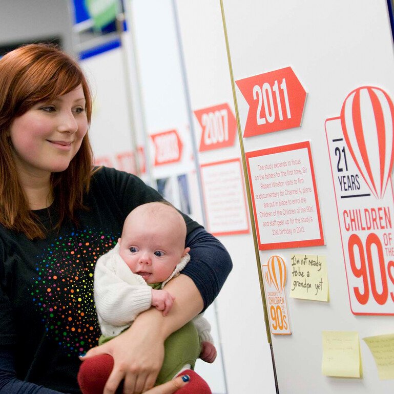 Young woman holding a baby looking at Children of the 90s timeline