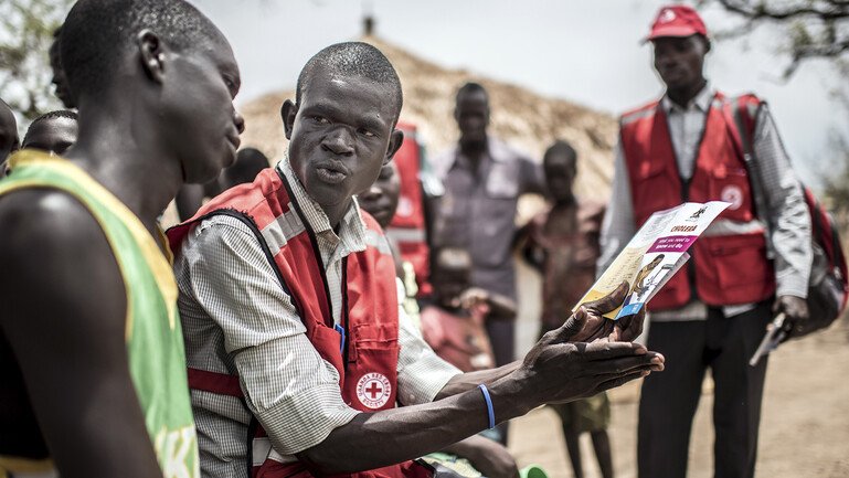 A Red Cross volunteer shows a cholera leaflet to refugees in a camp.