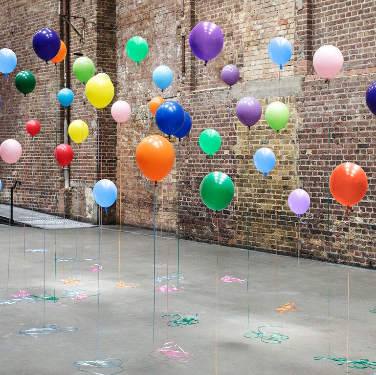 Different coloured balloons suspended in front of a brick wall