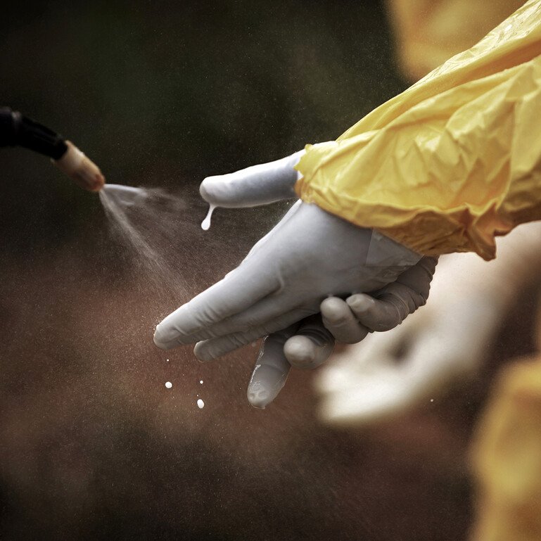 Chlorine is sprayed onto the hands of a health worker wearing yellow protective gloves.