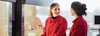 Two women wearing red lab coats talking to each other