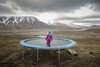 A girl stands on a trampoline in the middle of a mountainous landscape.