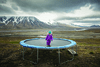 A girl stands on a trampoline in the middle of a mountainous landscape.